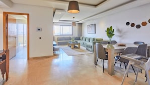 Uma sala de estar espaçosa com sofá, mesa de jantar e cadeiras, uma janela grande e um lustre.