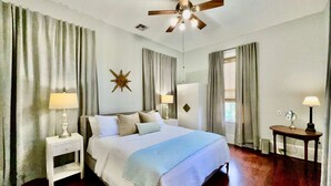 Habitación de hotel con cama, mesita de noche, ventilador de techo, decoración con estrellas y ventana con cortinas.