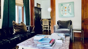 Un salón con un sofá de cuero, una mesa de centro de mármol con libros, una silla de madera y un cuadro en la pared.
