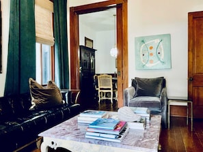 Ein Wohnzimmer mit einer Ledersofa, einem Marmortisch mit Büchern, einem Holzstuhl und einem Gemälde an der Wand.