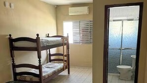 Una habitación con literas, una cama individual, un inodoro y una ventana con persianas.