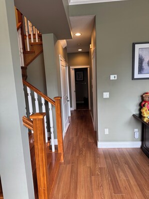 A hallway with wooden flooring, a staircase with white balusters, and a framed picture on the wall. - Surrey ( Fleetwood)Home (Surrey)