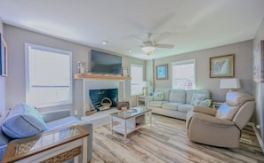 A living room with a fireplace, sofa, armchair, and a television. - Cozy Coastal Cottage - 1615 New River Inlet Rd. (North Topsail Beach)
