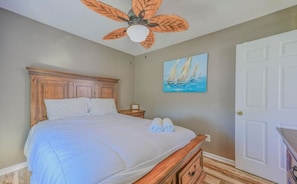 A bedroom with a wooden bed, a ceiling fan, a painting of sailboats, and a white door. - Cozy Coastal Cottage - 1615 New River Inlet Rd. (North Topsail Beach)