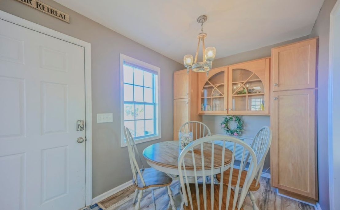 A dining area with a round table, white chairs, a chandelier, and wooden cabinets.