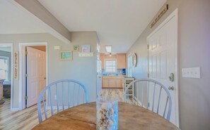 A dining area with a table and chairs, a kitchen in the background, and a door with a sign. - Cozy Coastal Cottage - 1615 New River Inlet Rd. (North Topsail Beach)