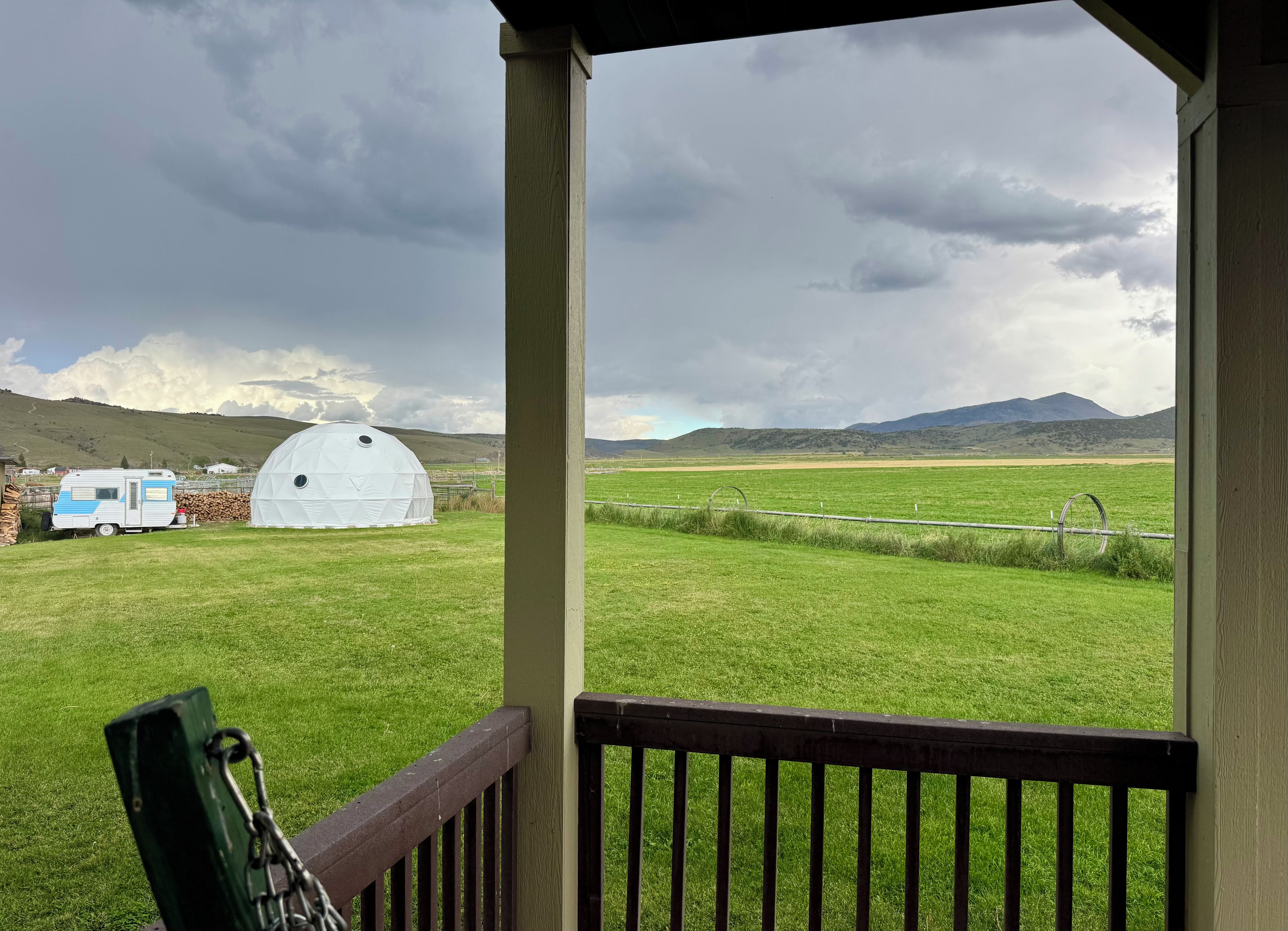 A view from a covered porch overlooking a grassy field with a white dome structure and a blue RV.