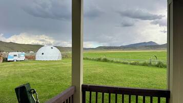 A view from a covered porch overlooking a grassy field with a white dome structure and a blue RV.