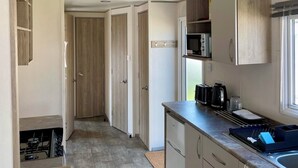 Une cuisine compacte équipée d’un micro-ondes, d’un grille-pain et d’une bouilloire sur le plan de travail, d’un petit évier et d’armoires en bois.