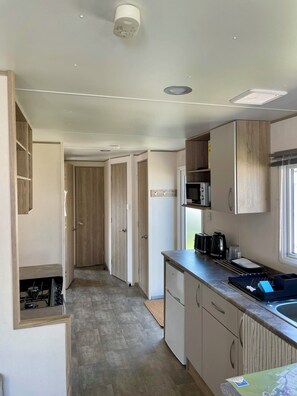 A compact kitchen with a microwave, toaster, and kettle on the counter, a small sink, and wooden cabinets.