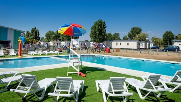 Une piscine bordée de chaises longues blanches et agrémentée d’un parasol coloré.