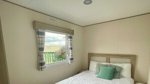 Une chambre à coucher avec un lit simple, une fenêtre avec des rideaux, une table de chevet et une commode.