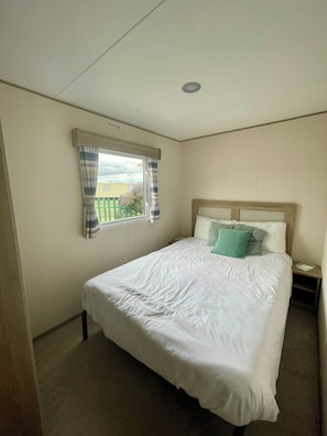 A bedroom with a single bed, a window with curtains, a nightstand, and a bedside table.