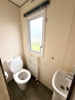 Une petite salle de bain propre, équipée de toilettes, d’une fenêtre, d’un radiateur et d’un lavabo.