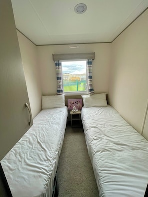 Una habitación de hotel pequeña y con una cama doble, una ventana con cortinas, una mesita con lámpara y vista a un patio de juegos.