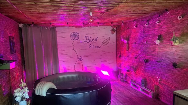 Um quarto com uma área de estar circular preta, teto de madeira e parede com um desenho floral e a frase 'Bien être'.