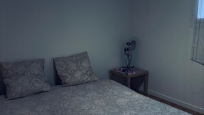 Quarto com cama, duas almofadas, mesa de cabeceira com abajur e janela.