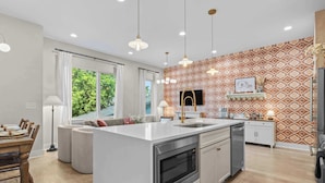 Une cuisine moderne dotée d’un îlot central, de luminaires suspendus et d’un revêtement mural décoratif.