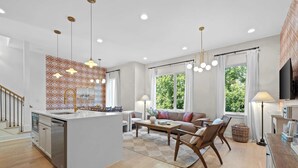 Une cuisine moderne dotée d’un îlot central, d’un coin repas avec un canapé et des chaises, et de grandes fenêtres offrant une vue sur la verdure.