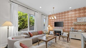 Un salon comprenant un canapé, des fauteuils, une table basse, une cheminée et un téléviseur fixé au mur.