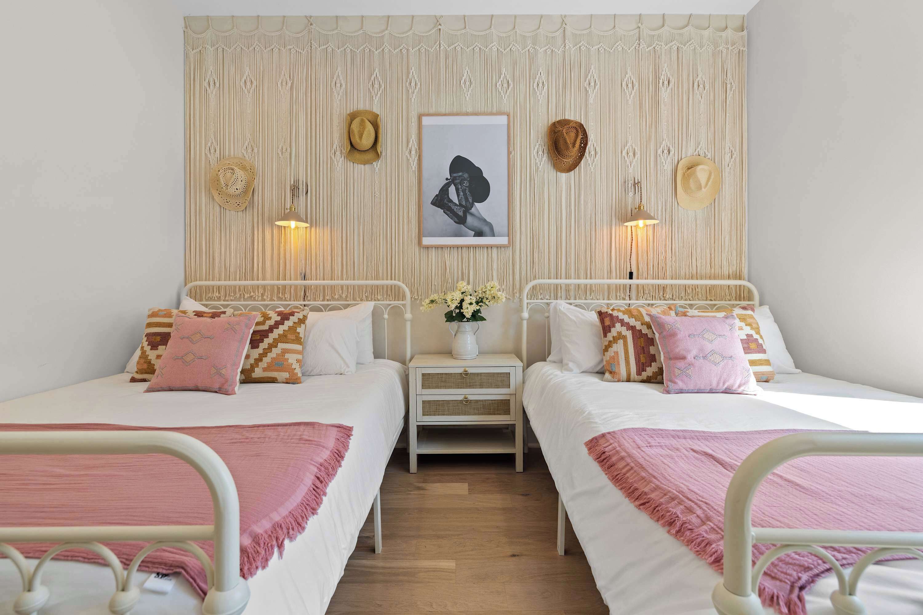 A twin room with two beds, a bedside table with a vase of flowers, and a wall-mounted picture.