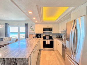 A modern kitchen with a central island, stainless steel appliances, and a view to the beach. - Vacation Villas #635 Renovated 6th Floor Beachfront Condo (Fort Myers Beach)