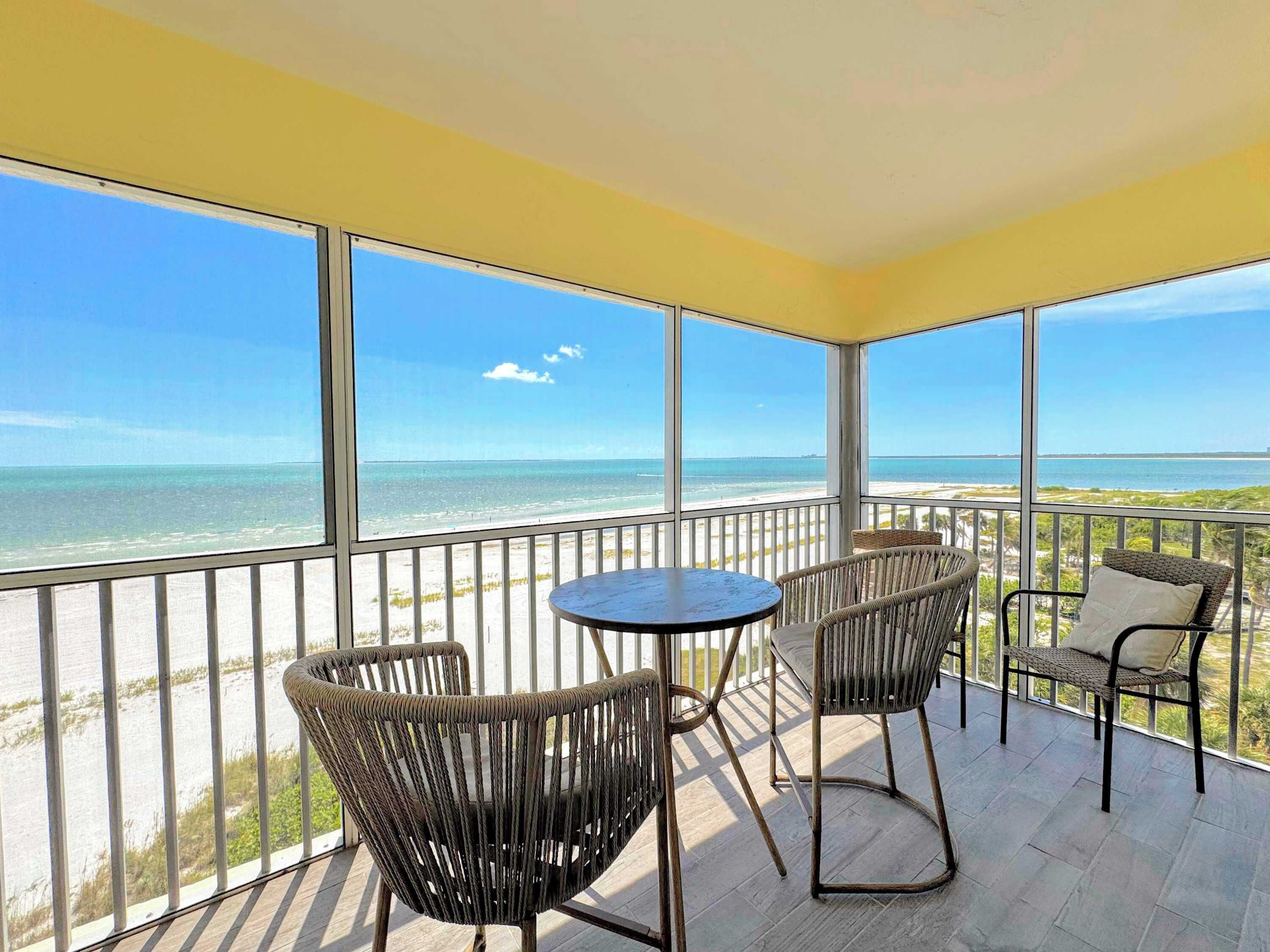 A balcony with a view of the ocean, wicker chairs, a small round table, and a railing.