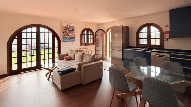 A spacious living area with a glass dining table, a sofa, and a kitchen with a refrigerator and cabinets.