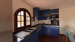 A kitchen with a large window, blue cabinets, a built-in oven, and a dining area with a table and chairs.