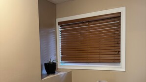 Ein Schlafzimmer mit Fenster, Nachttisch mit Lampe, Topfpflanze und Bett.