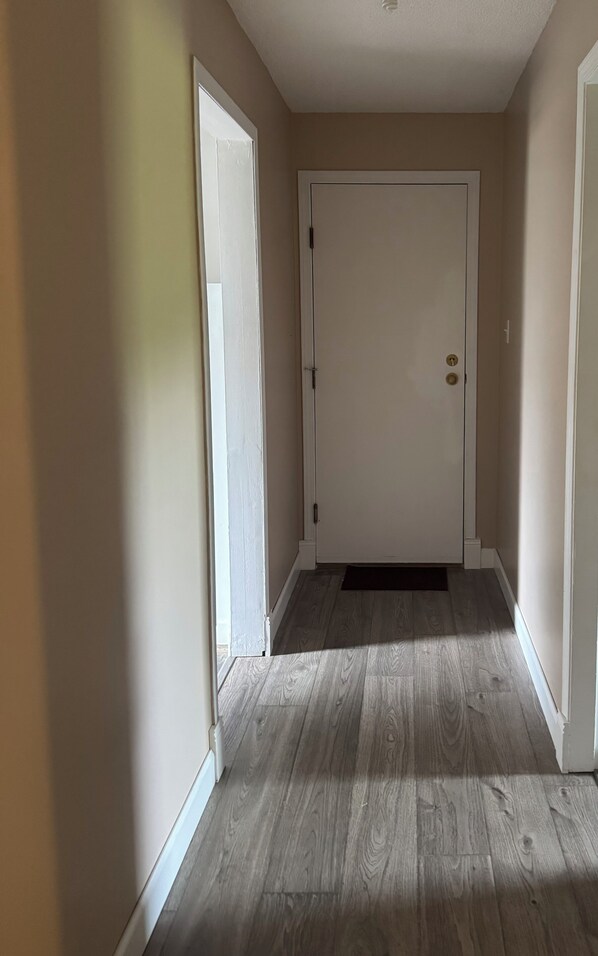 A hallway with a wooden floor, a white door, and beige walls. - Cozy guest suite, located centrally. (Nanaimo)