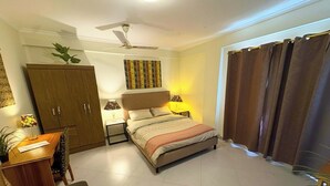 A bedroom with a bed, a desk, a chair, a wardrobe, a ceiling fan, and a window with curtains.