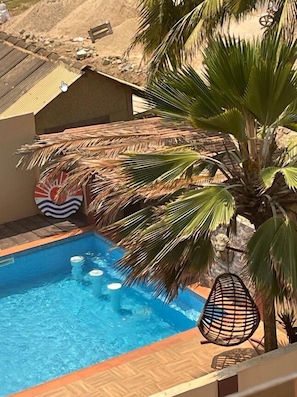 A swimming pool with clear blue water, surrounded by palm trees and a thatched roof structure.