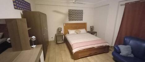 Un dormitorio con cama, sofá azul, armario, ventilador de techo y un tapiz de pared estampado.