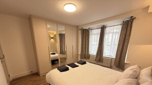Une chambre à coucher avec un lit, une armoire, un miroir et une fenêtre avec des rideaux.