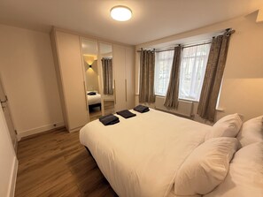 Ein Schlafzimmer mit Bett, Kleiderschrank, Spiegel und einem Fenster mit Vorhängen.