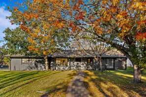 A single-story house with a front yard, a pathway leading to the entrance, and a tree with autumn leaves. - Austin Retreat with Private Pool l Mins to Downtown! (Austin)