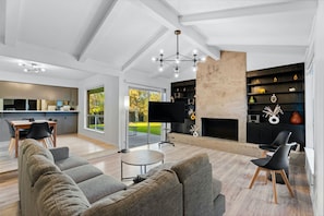 Una sala de estar moderna con un sofá, sillas, una chimenea y una cocina al fondo.