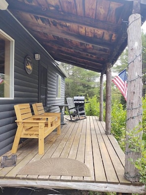 Eine Holzterrasse mit Sitzgelegenheiten im Freien, einem Grill und einer amerikanischen Flagge.