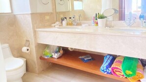 Un baño con lavamanos doble, un espejo, toallero y repisa con artículos de aseo.
