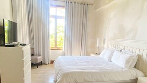 Un dormitorio con cama, televisor, cómoda y ventana con cortinas.