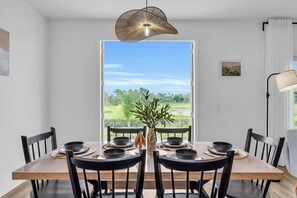 Ein Essbereich mit einem Tisch für vier Personen, einer Hängelampe und Blick auf eine grüne Landschaft durch ein großes Fenster.