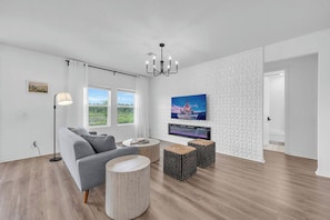 Ein modernes Wohnzimmer mit einem grauen Sofa, einem runden Couchtisch und einem Flachbildfernseher, der an einer strukturierten Wand angebracht ist.