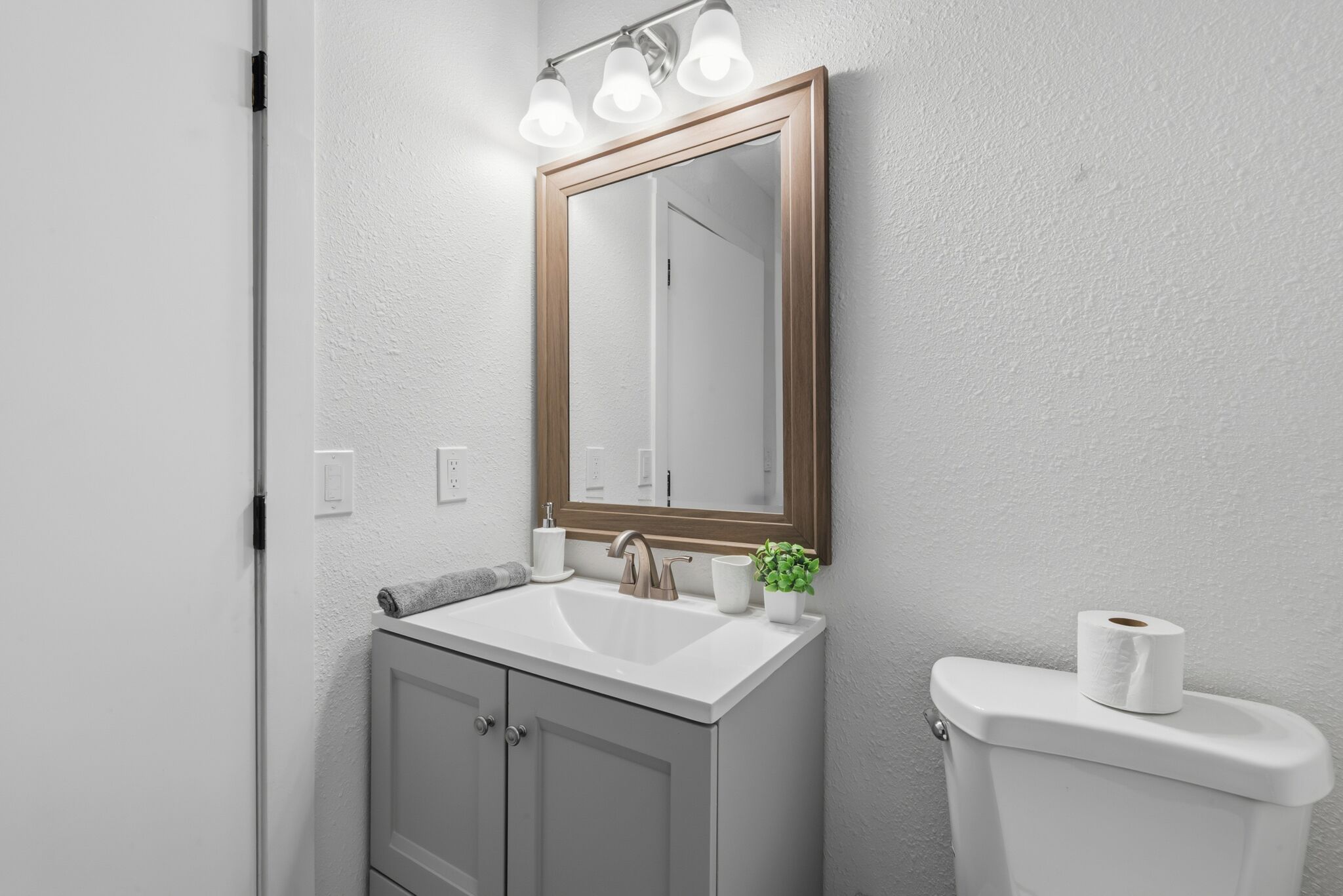 Une salle de bain avec un lavabo blanc, un miroir avec éclairage intégré, des toilettes et une plante.