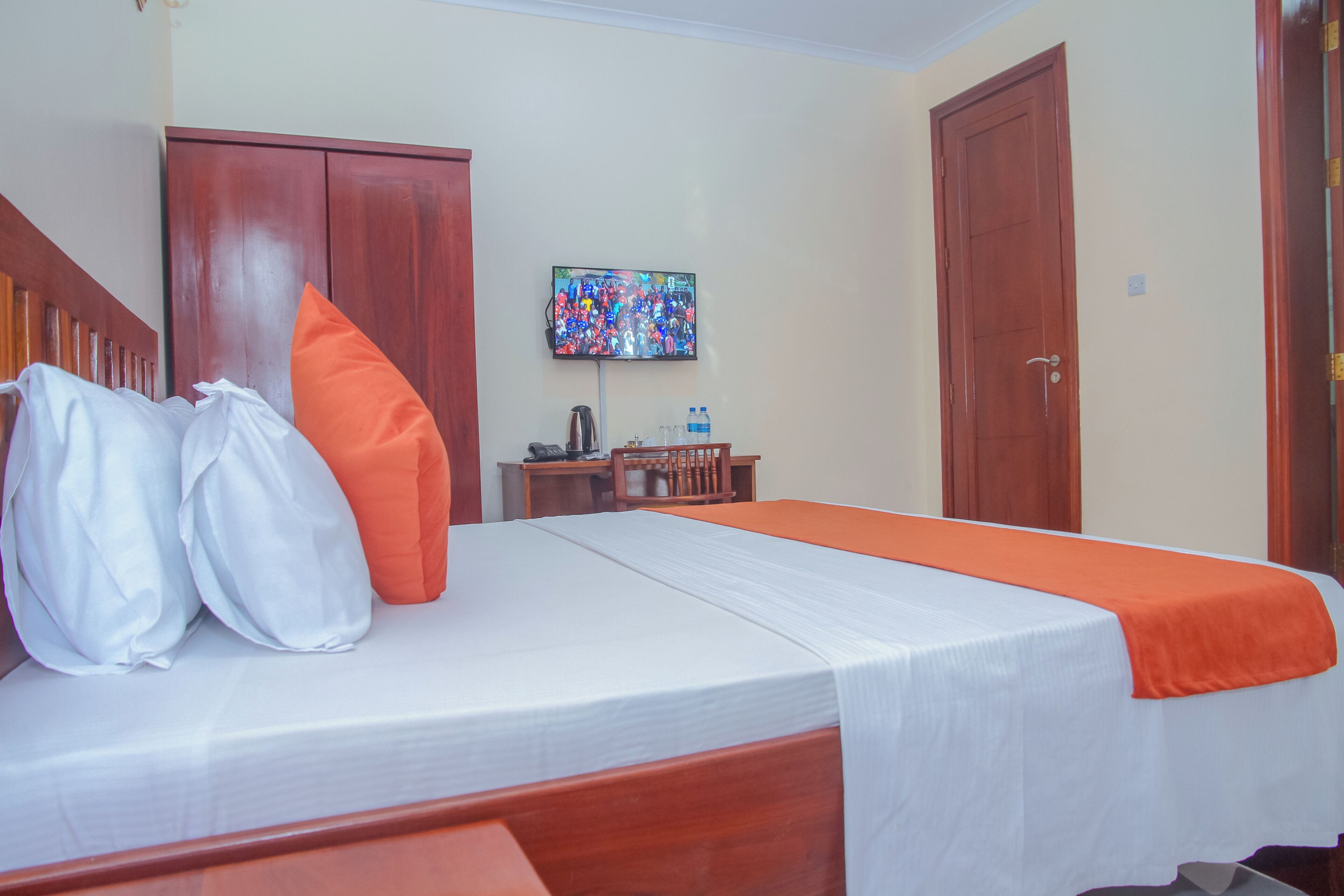 A hotel room with a bed, pillows, a TV, a desk with a chair, and a wardrobe.