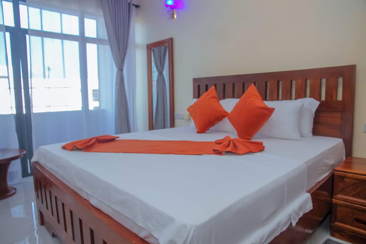Una cama bien hecha con sábanas blancas y almohadas naranjas, un cabecero de madera y una mesita de noche con cajones.