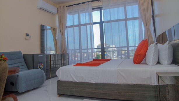 Habitación de hotel moderna con una cama grande, un sofá, una mesita y vistas a la ciudad a través de amplios ventanales.