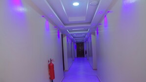 Un pasillo largo y estrecho con un extintor en la pared izquierda, un techo con iluminación empotrada y una puerta al final.