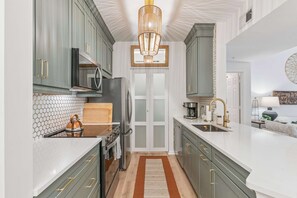 A modern kitchen with grey cabinets, a central island, and a hanging light fixture. - Coastal Sage by Redfern (St. Simons Island)