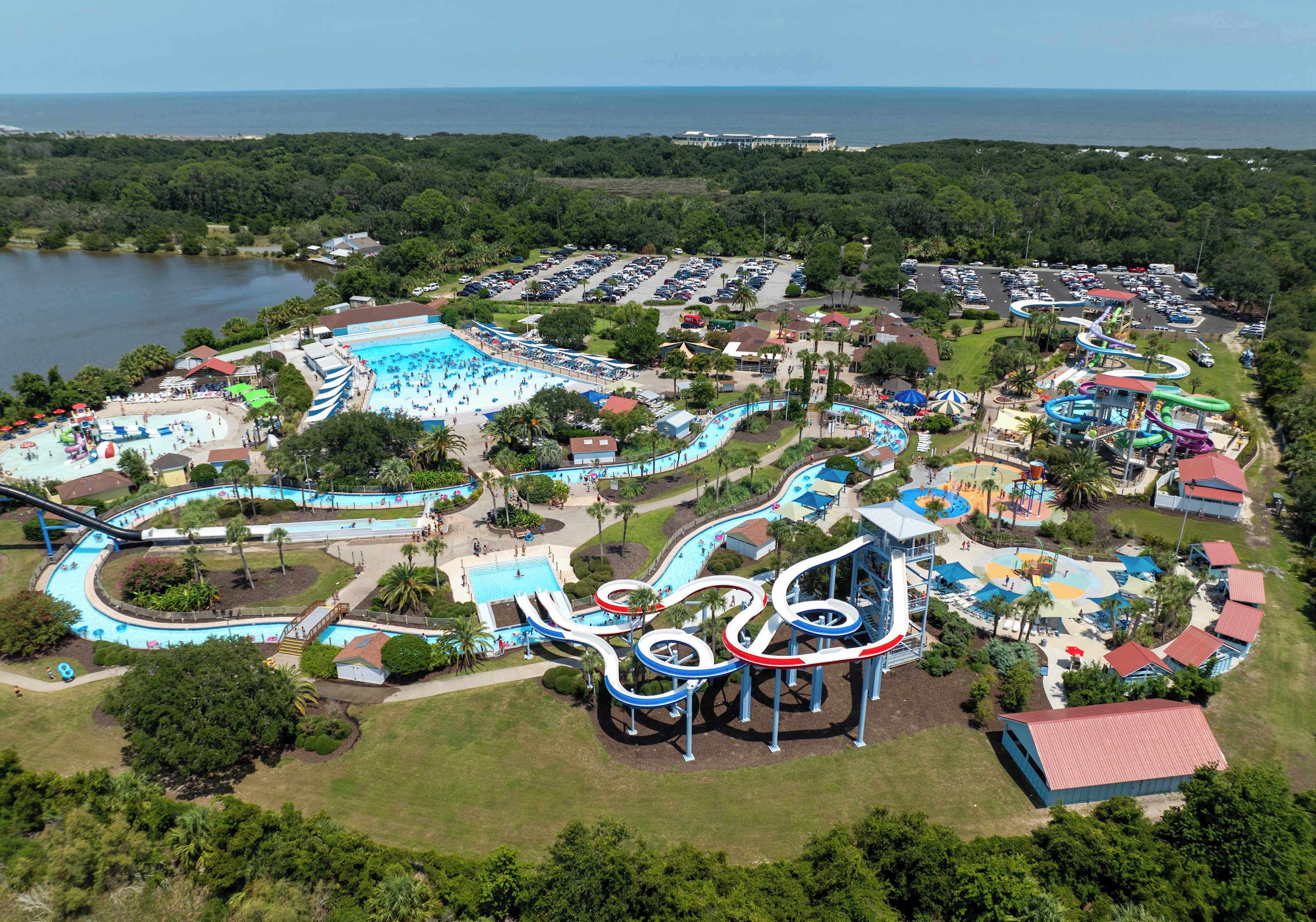 An aerial view of a water park with multiple slides and pools, surrounded by parking and greenery.